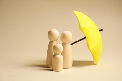 Photo of Human figures under umbrella on beige background. Insurance concept