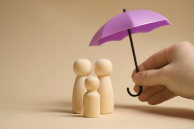 Photo of Woman holding umbrella over human figures on beige background, closeup. Insurance concept