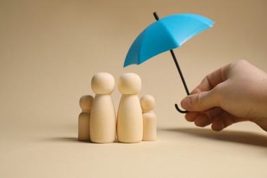 Photo of Woman holding umbrella over human figures on beige background, closeup. Insurance concept