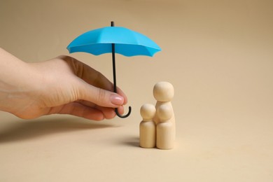 Photo of Woman holding umbrella over human figures on beige background, closeup. Insurance concept