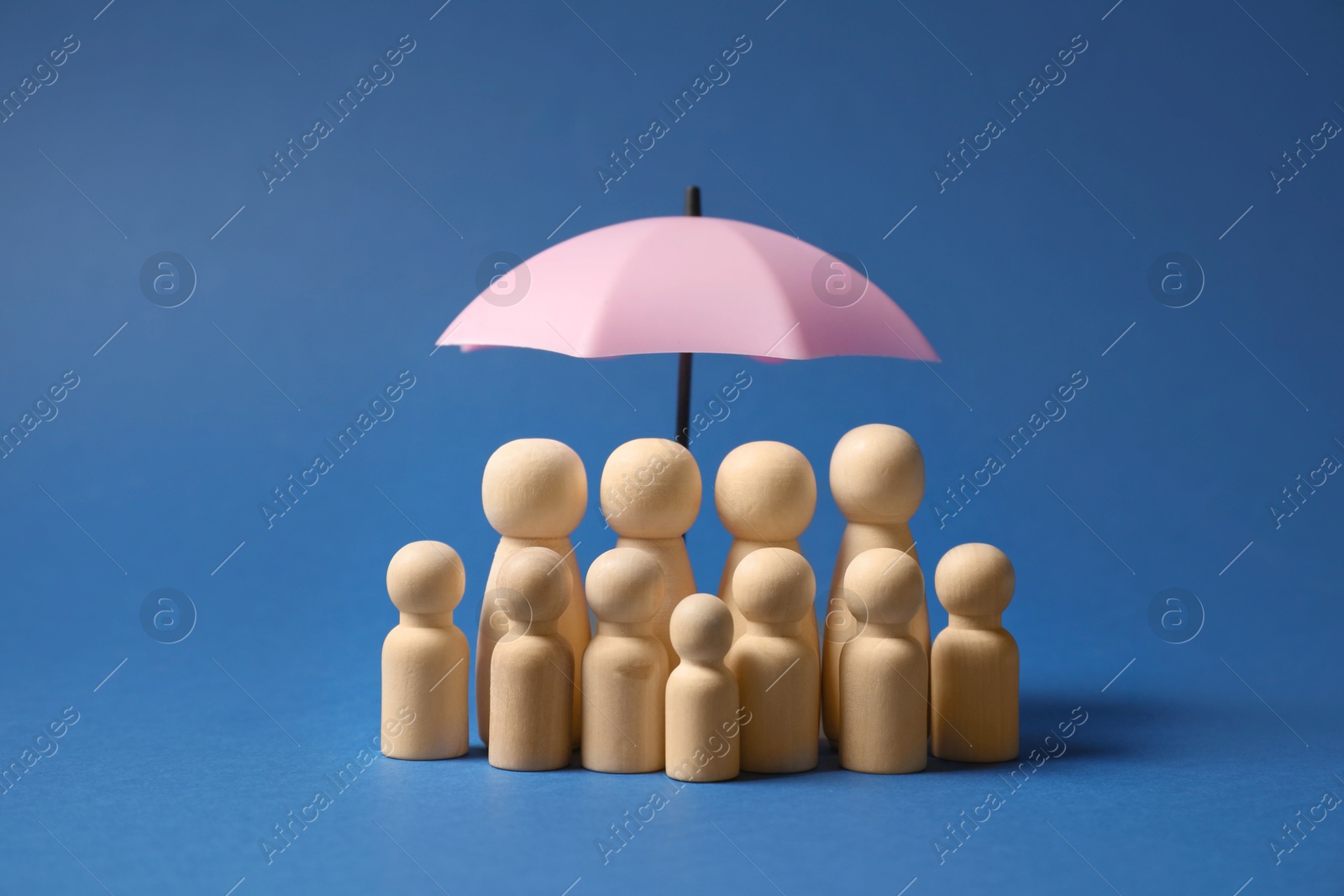 Photo of Human figures under umbrella on blue background. Insurance concept