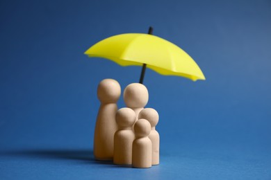 Photo of Human figures under umbrella on blue background. Insurance concept