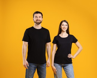 Photo of Woman and man wearing blank black t-shirts on orange background. Mockup for design