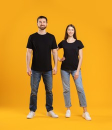 Photo of Woman and man wearing blank black t-shirts on orange background. Mockup for design