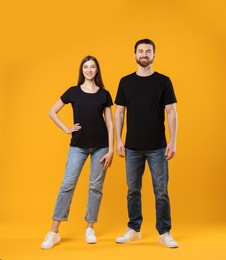 Photo of Woman and man wearing blank black t-shirts on orange background. Mockup for design