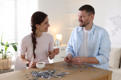 Photo of Happy couple solving puzzle together at wooden table indoors