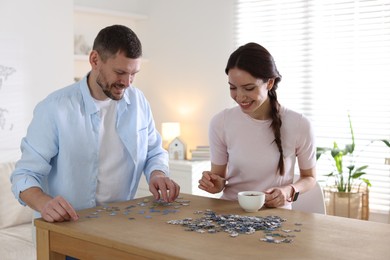 Photo of Happy couple solving puzzle together at wooden table indoors