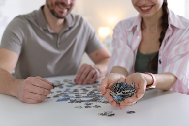 Photo of Couple solving puzzle together at white table indoors, closeup