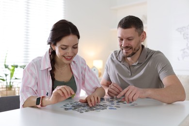 Photo of Happy couple solving puzzle together at white table indoors