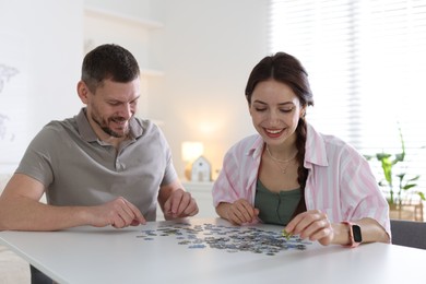 Photo of Happy couple solving puzzle together at white table indoors