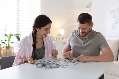 Photo of Happy couple solving puzzle together at white table indoors