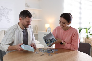 Photo of Happy couple solving puzzle together at wooden table indoors