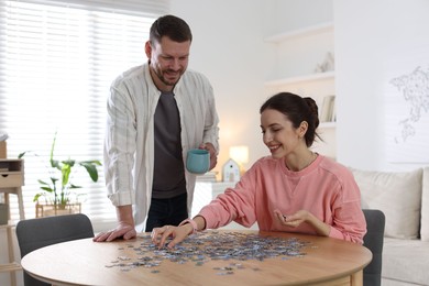 Photo of Happy couple solving puzzle together at wooden table indoors