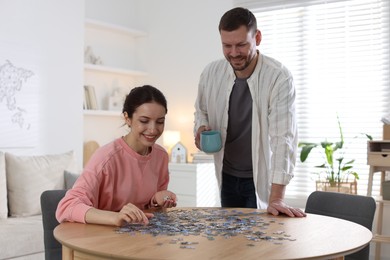 Photo of Happy couple solving puzzle together at wooden table indoors