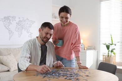 Photo of Happy couple solving puzzle together at wooden table indoors