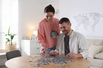 Photo of Happy couple solving puzzle together at wooden table indoors