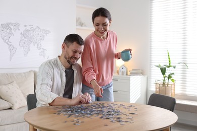 Photo of Happy couple solving puzzle together at wooden table indoors