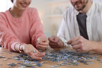 Photo of Couple solving puzzle together at wooden table indoors, closeup