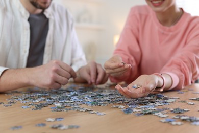 Photo of Couple solving puzzle together at wooden table indoors, closeup