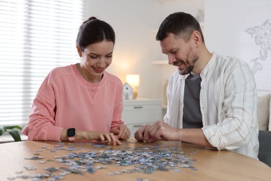 Photo of Happy couple solving puzzle together at wooden table indoors