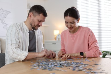 Photo of Happy couple solving puzzle together at wooden table indoors