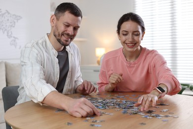 Photo of Happy couple solving puzzle together at wooden table indoors