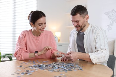 Photo of Couple solving puzzle together at wooden table indoors