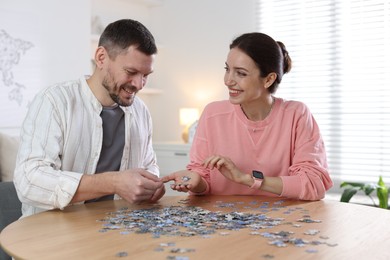 Photo of Couple solving puzzle together at wooden table indoors