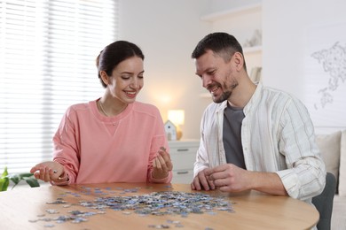 Photo of Couple solving puzzle together at wooden table indoors