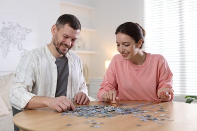 Photo of Couple solving puzzle together at wooden table indoors