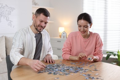 Photo of Couple solving puzzle together at wooden table indoors