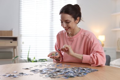 Photo of Happy woman solving puzzle at wooden table indoors, space for text