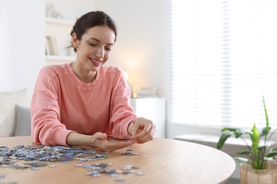 Photo of Happy woman solving puzzle at wooden table indoors, space for text