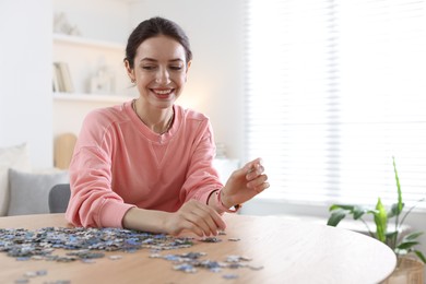 Photo of Happy woman solving puzzle at wooden table indoors, space for text