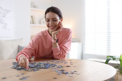 Photo of Happy woman solving puzzle at wooden table indoors, space for text