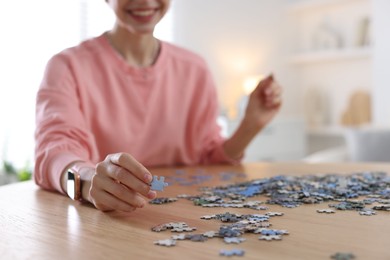 Photo of Woman solving puzzle at wooden table indoors, closeup