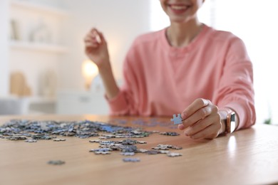 Photo of Woman solving puzzle at wooden table indoors, closeup