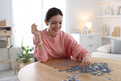 Photo of Happy woman solving puzzle at wooden table indoors