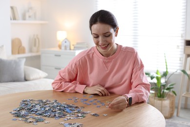 Photo of Happy woman solving puzzle at wooden table indoors