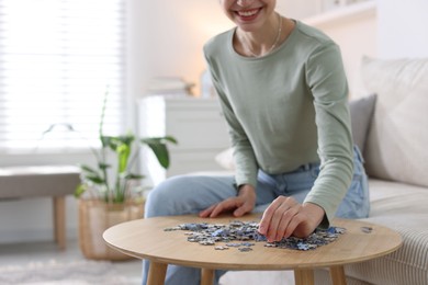 Photo of Woman solving puzzle at wooden table indoors, closeup. Space for text