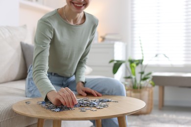 Photo of Woman solving puzzle at wooden table indoors, closeup. Space for text