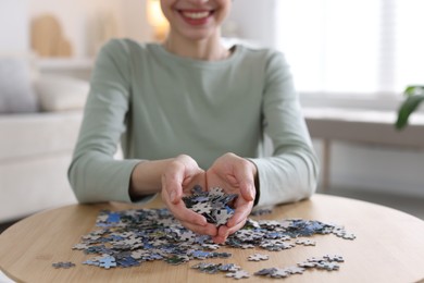 Photo of Woman solving puzzle at wooden table indoors, closeup