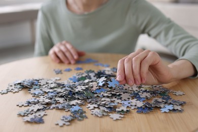 Photo of Woman solving puzzle at wooden table indoors, closeup