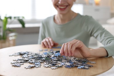 Photo of Woman solving puzzle at wooden table indoors, closeup