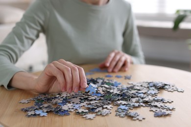 Photo of Woman solving puzzle at wooden table indoors, closeup