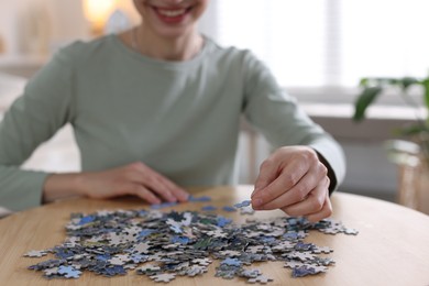 Photo of Woman solving puzzle at wooden table indoors, closeup