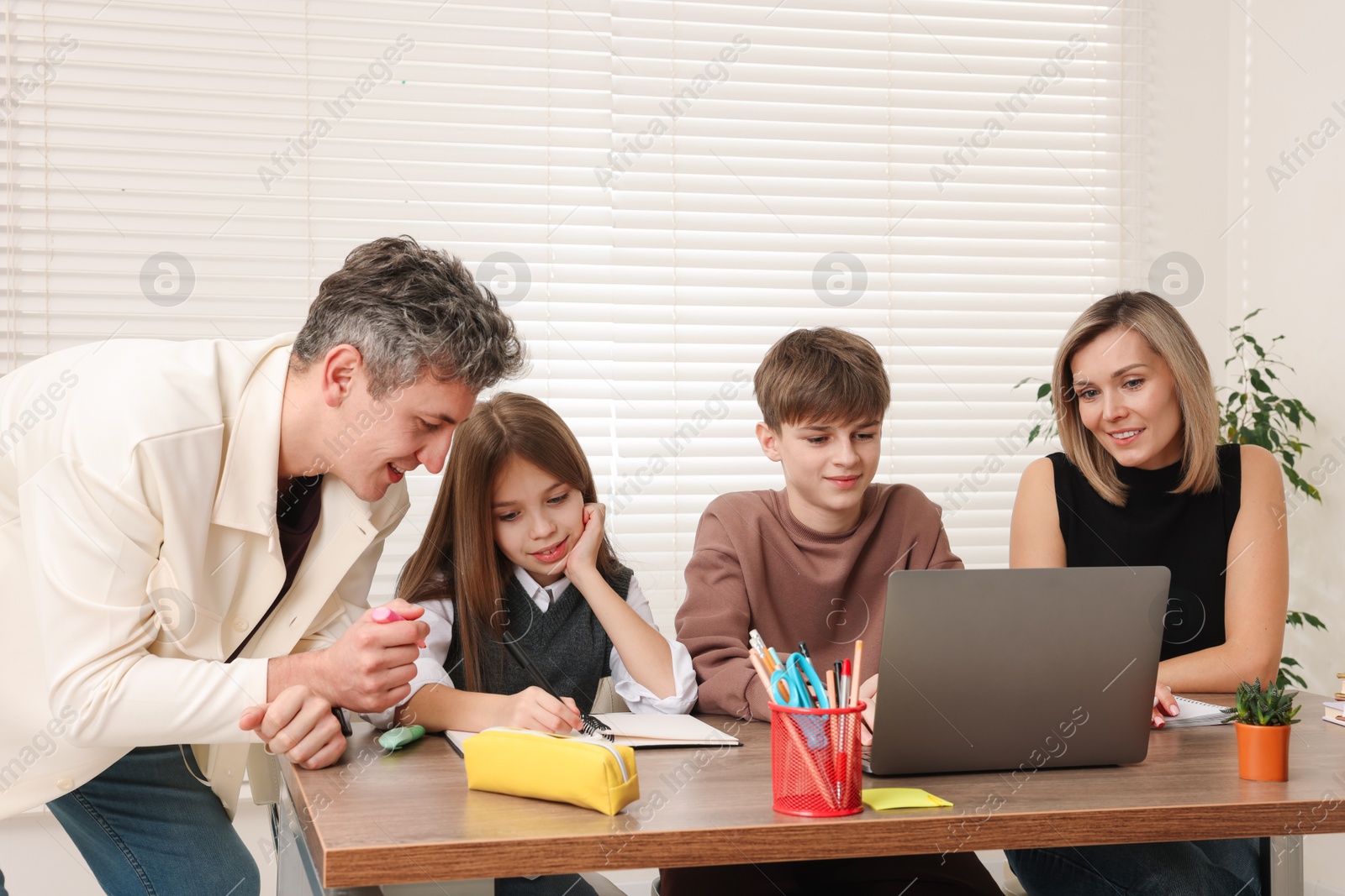 Photo of Parents and their children doing homework with laptop at table indoors