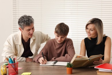 Photo of Parents helping their son with homework at table indoors