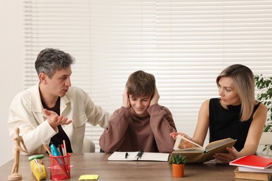 Photo of Parents and their stressful son doing homework at table indoors