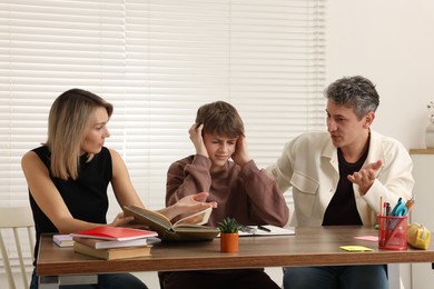 Photo of Parents and their stressful son doing homework at table indoors